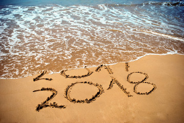 New Year 2018 is coming concept - inscription 2017 and 2018 on a beach sand, the wave is covering digits 2017. New Year 2018 celebration on New Year`s Eve tropical island travel tour.