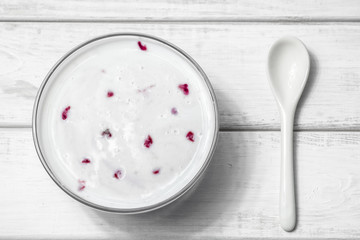 Berry yogurt in a plate with a spoon on a white wooden background. 