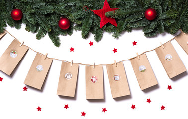 Handmade tinkered advent calendar with paper bags and stickers hanging from fir branches and red...