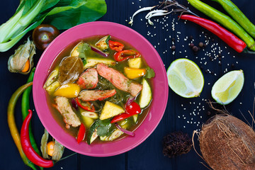 Fototapeta na wymiar Appetizing green curry soup with chicken and rice noodles, flat lay on dark background with ingredients. Pan-Asian, thai food, oriental cuisine, food background