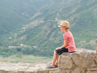 Boy in a hat sitting on stones on a background of green mountains