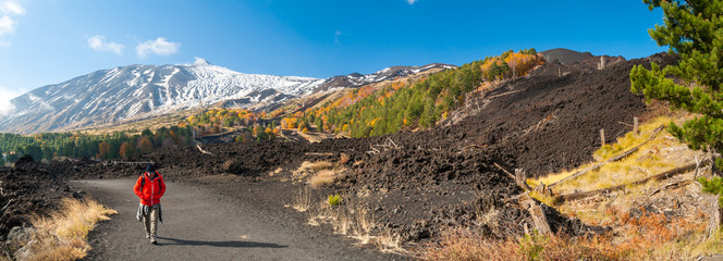 Mount Etna, Italy: panorama of the northern side of the volcano and a hiker walking on a lavic pathway - obrazy, fototapety, plakaty
