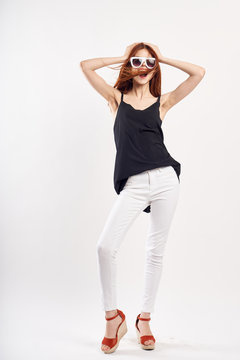 Girl is happy and posing in black top and white pants on a light background