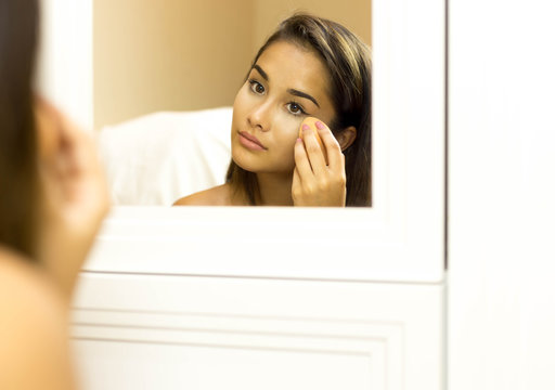 Mixed Race Young Woman Applying Foundation On With Sponge Looking In The Mirror