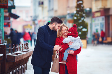 happy family, mother, father and baby walking through the winter snowy city street