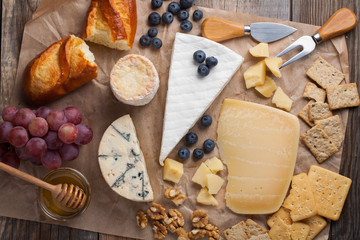 Tasting cheese dish on a wooden plate. Food for wine and romantic, cheese delicatessen on a wooden rustic table. Top view