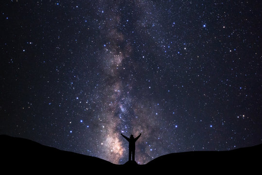 Milky way galaxy with stars and silhouette of a standing happy man, Long exposure photograph, with grain.