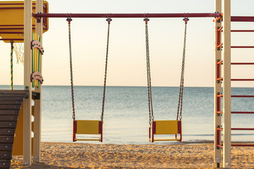 Two swings of children's playgrounds on the beach.