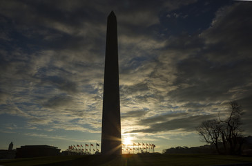 Sun moving behind Washington Monument surrounded by US flags against blue sky