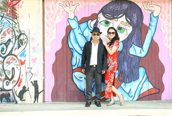 Asian couple in chinese dress and black eyeglasses standing against the street art wall