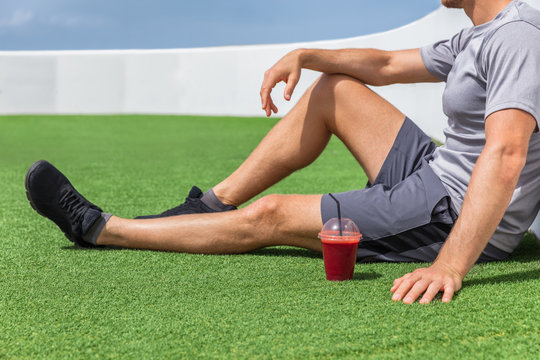 Juice Smoothie Sport Man Relaxing Enjoying Post Workout Morning Breakfast Sitting On Outdoor Grass At Home Or Fitness Gym. Athlete Drinking Red Fruit Smoothie Drink.