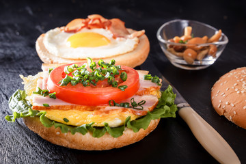 Sandwich with fried egg, bacon, tomato, greens. Breakfast with fried potatoes and mushrooms. Black background
