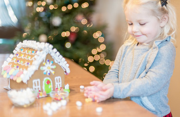 Little girl decorating holiday gingerbread house at Christmas
