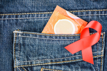 Condom pack and red awareness ribbon on blue jeans pocket. AIDS and HIV awareness concept.