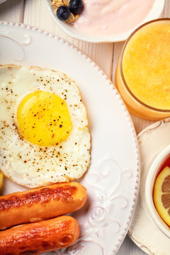 Breakfast of sunny side up eggs, sausages, orange juice, and fruits, top view, vertical composition