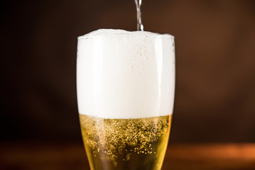 Cold beer being poured into the glass with frothy foam