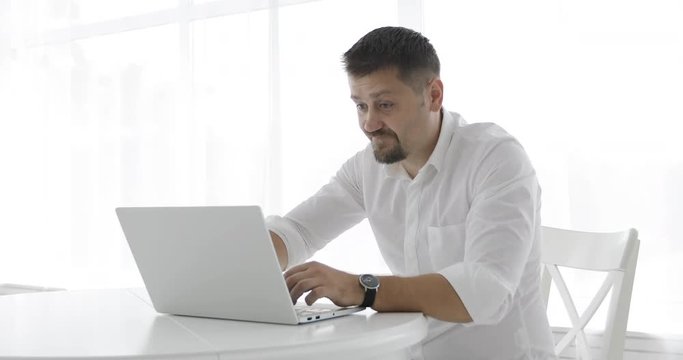Stylish businessman in a white shirt nervously typing on a laptop and closing it.