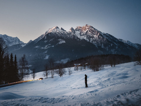 Mann stht in winterlicher Landschaft morgens vor einem Berg w&auml;hrend die Sonne auf geht
