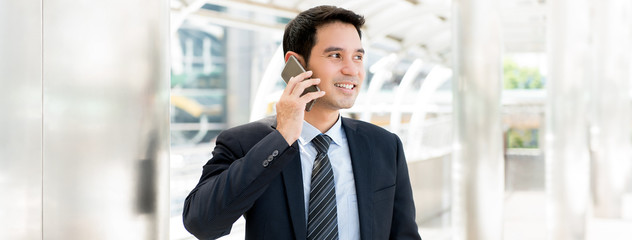 Handsome Asian businessman calling on smartphone while walking in the city