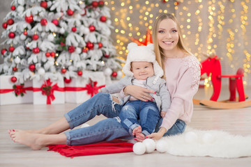 happy family mother and baby little son playing home on Christmas holidays.Toddler with mom in the festively decorated room with Christmas tree. Portrait of mother and baby boy in casual clothes
