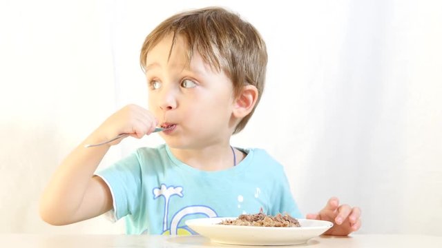 A child eats food with a fork from a plate on a white background.