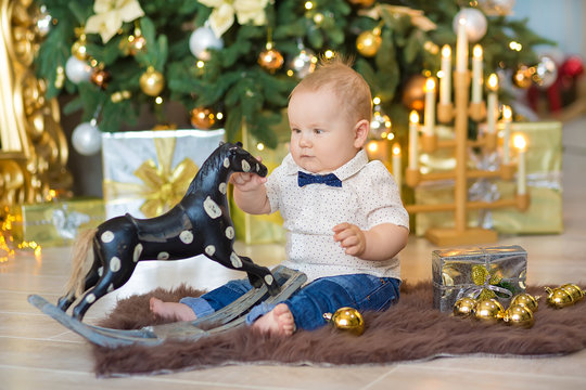 Beautiful little baby boy celebrates Christmas. New Year's holidays. Baby in a Christmas costume casual clothes with gifts on fur close to new year tree in studio decorations.