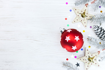 red glass ball with wooden stars and christmas fir branches on festive background with sparkling confetti