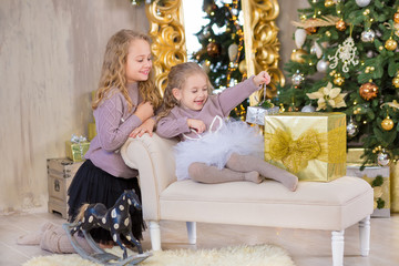 Christmas portrait of two beautyful cute girls Smiling sisters friends and xmas luxury green white tree in unique interior studio with huge golden mirror and fur