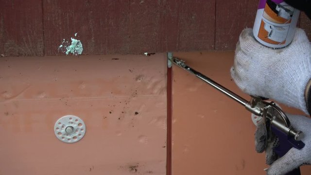 Worker hands with fixfoam glue fixing slots of polystyrene on house foundation