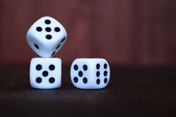 Heap of three white plastic dices on brown wooden board background. Six sides cube with black dots. Numbers 1, 3, 5, 6.