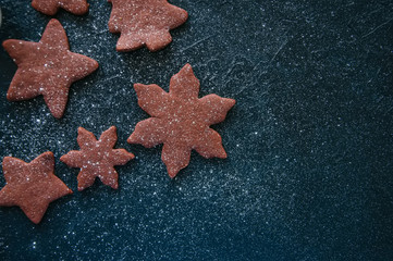 Different shapes of chocolate gingerbread cookies sprinkled with powdered sugar on a black stone backdrop.