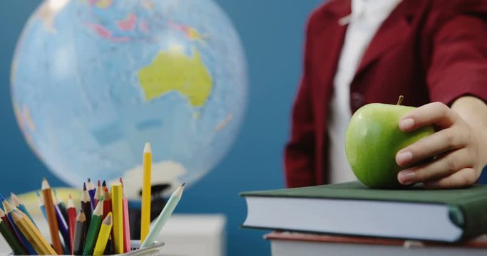 Close up of the school stuff and a green apple on textbooks being taken by kid's hand. Globe on the background. Inside