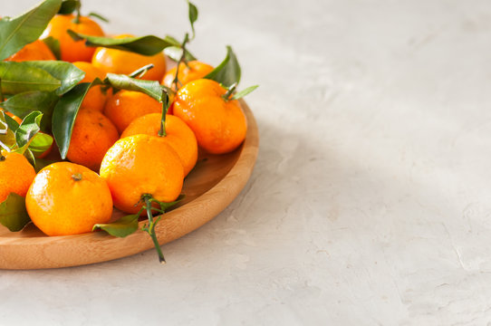 Plate of fresh and juicy tangerines with leaves on a white stone background. Close up and copy space. © galiyahassan