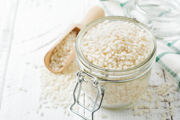 Raw  White rice variety Arborio for Italian risotto dishes in glass jar on  white concrete or stone background. Selective focus. Copy space.