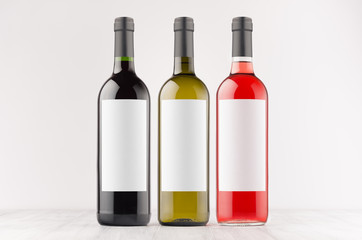 Three wine bottles - red, green, black - with blank white labels on white wooden board, mock up. Template for advertising, design, branding identity.