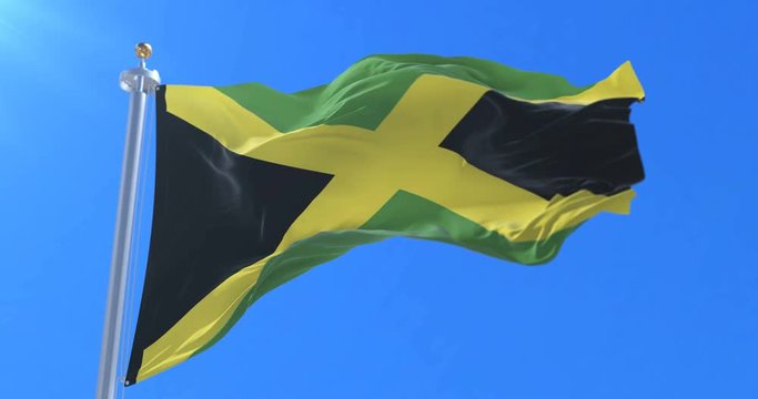 Flag of Jamaica waving at wind with blue sky in slow, loop