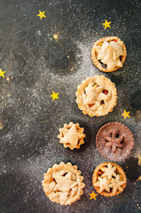 Different sizes of traditional Christmas dessert - Mince pies. Vanilla and chocolate pastry. Black backdrop.Top view.