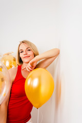 Young blonde woman in red t-shirt is smiling at the background of golden balloons. Celebrating the New Year, Christmas, Birthday Party. Close up