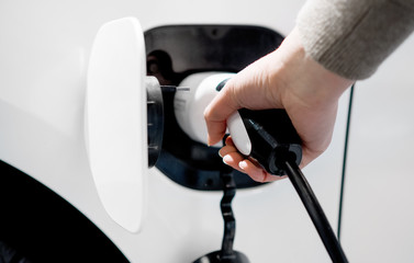 Hand holding electric plug for charging electric car.