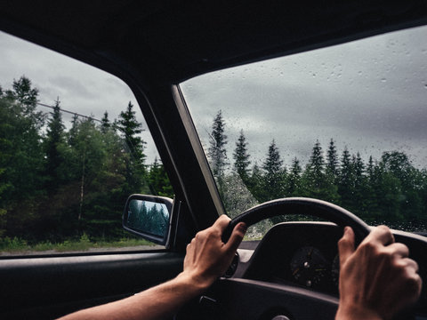 roadtrip moment im inneren eines autos mit h&auml;nden am lenkrad halb offenem fenster in waldumgebung und regen