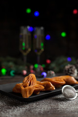 New Year's still-life. Glasses with champagne, New Year's lights, Christmas tree and sweet pastry. On a black plate