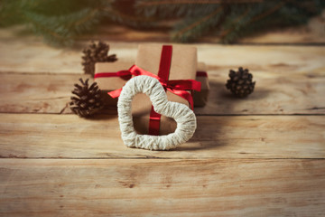 Gift boxes tied with red ribbon, heart handmade and fir cones on a wooden background