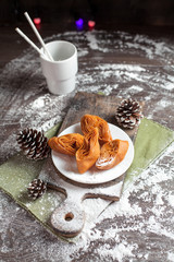holiday sweets on a New Year's table on a white plate, bumps and a cup of cocoa, a green napkin and New Year's lights on a dark background
