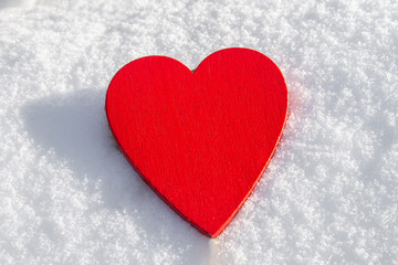 In the snow lies a red heart made of wood. Template for a holiday card with a white texture and free space for text.