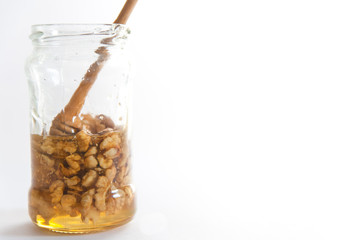 Wooden honey dipper in transparent jar filled with mixed  honey and walnut isolated on white background.