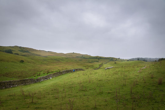 Hiker walking the Dales Way in the green and vast moorlands of England in moddy weather