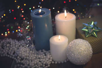 A festive still life with a light blue and two white candles of different size and a handcrafted gift box with a turquoise bow,white pearl beads on a colored wooden surface. Dark Christmas background