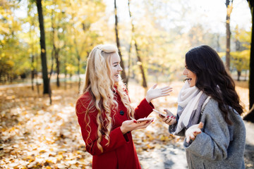 Portrait of a two laughing women talking outdoors in autumn park