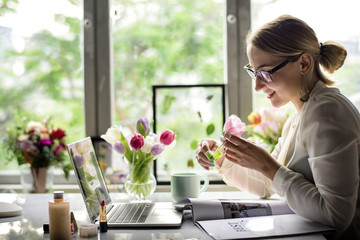 Woman smelling a flower in the office - obrazy, fototapety, plakaty