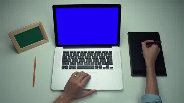 Top view male hands using graphic tab and laptop with green screen at white desk